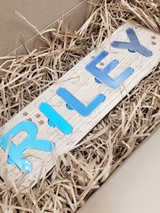 Engraved name puzzle for kids featuring blue acrylic letters spelling 'Riley', surrounded by decorative wood-themed illustrations.