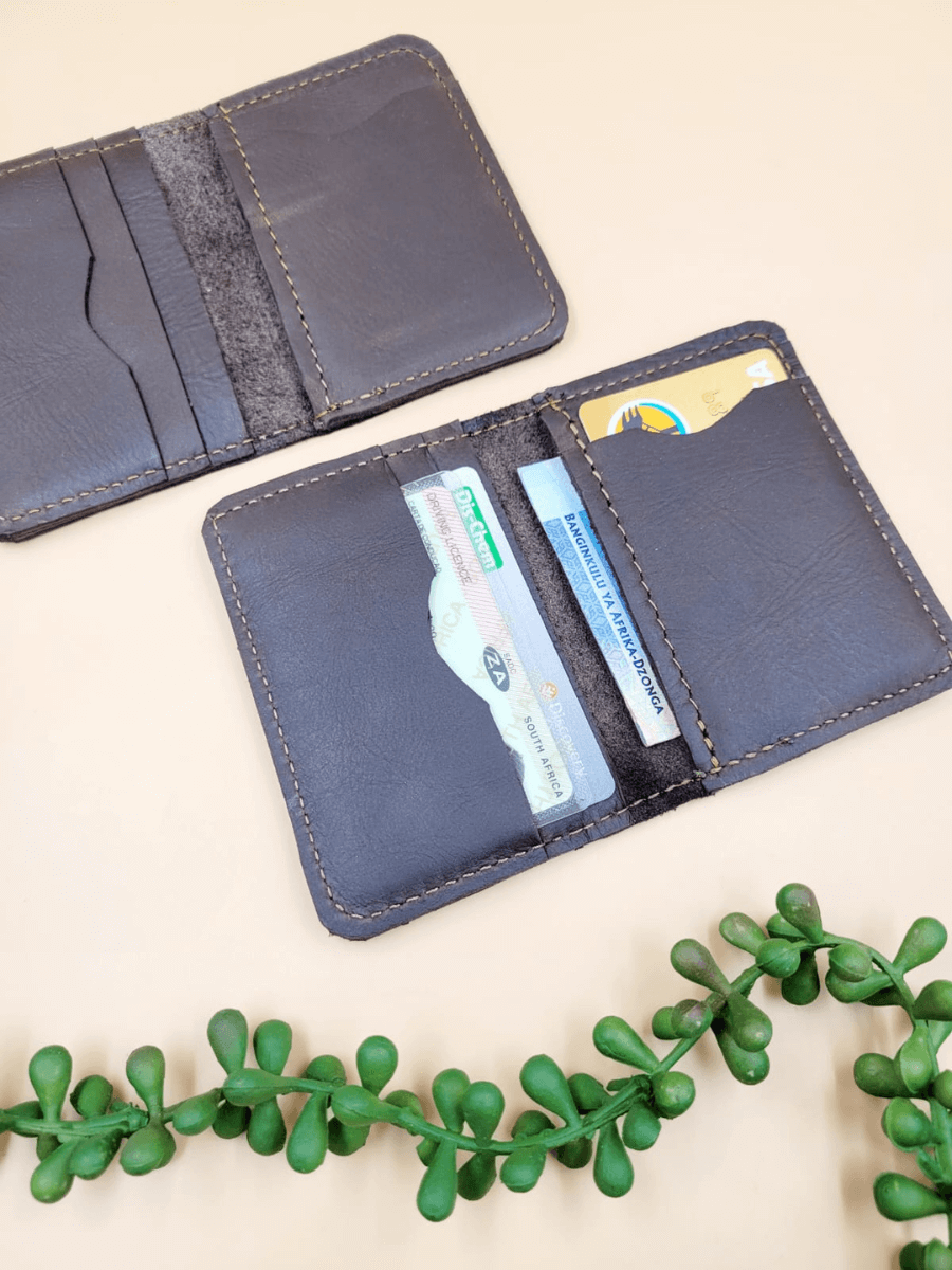 Open personalised men's leather bi-fold wallet on beige background with green plant, showing card slots and bill compartments.