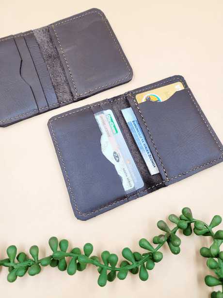 Open personalised men's leather bi-fold wallet on beige background with green plant, showing card slots and bill compartments.