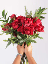 Hand holding a beautiful bouquet of classic red roses with greenery, perfect for Valentine's Day.