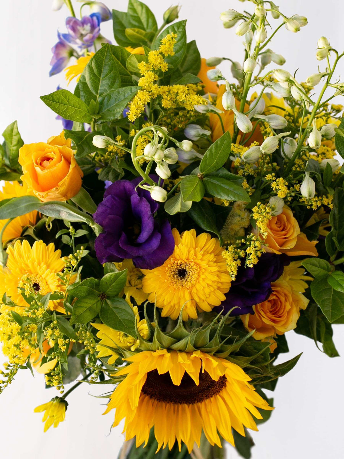 Colorful bunch of seasonal flowers in blues and yellows with sunflowers, roses, and foliage in a vibrant arrangement.