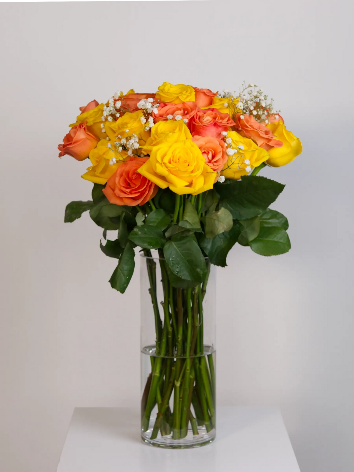 Orange and yellow rose bouquet with gypsophila in tall glass vase