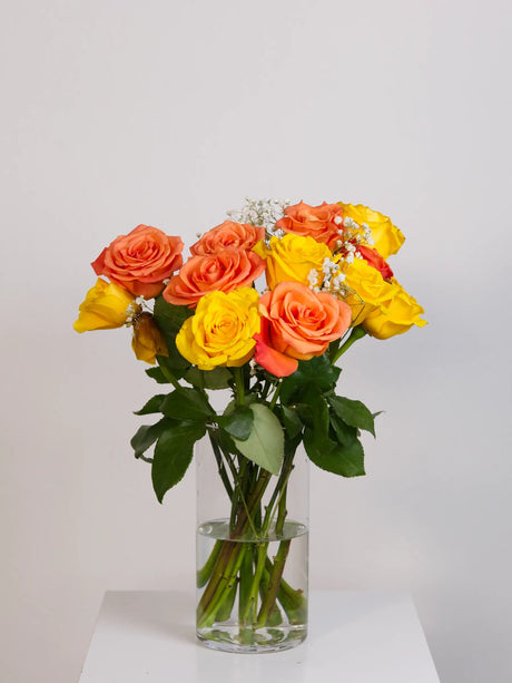 Orange and yellow rose bouquet with gypsophila in tall glass vase