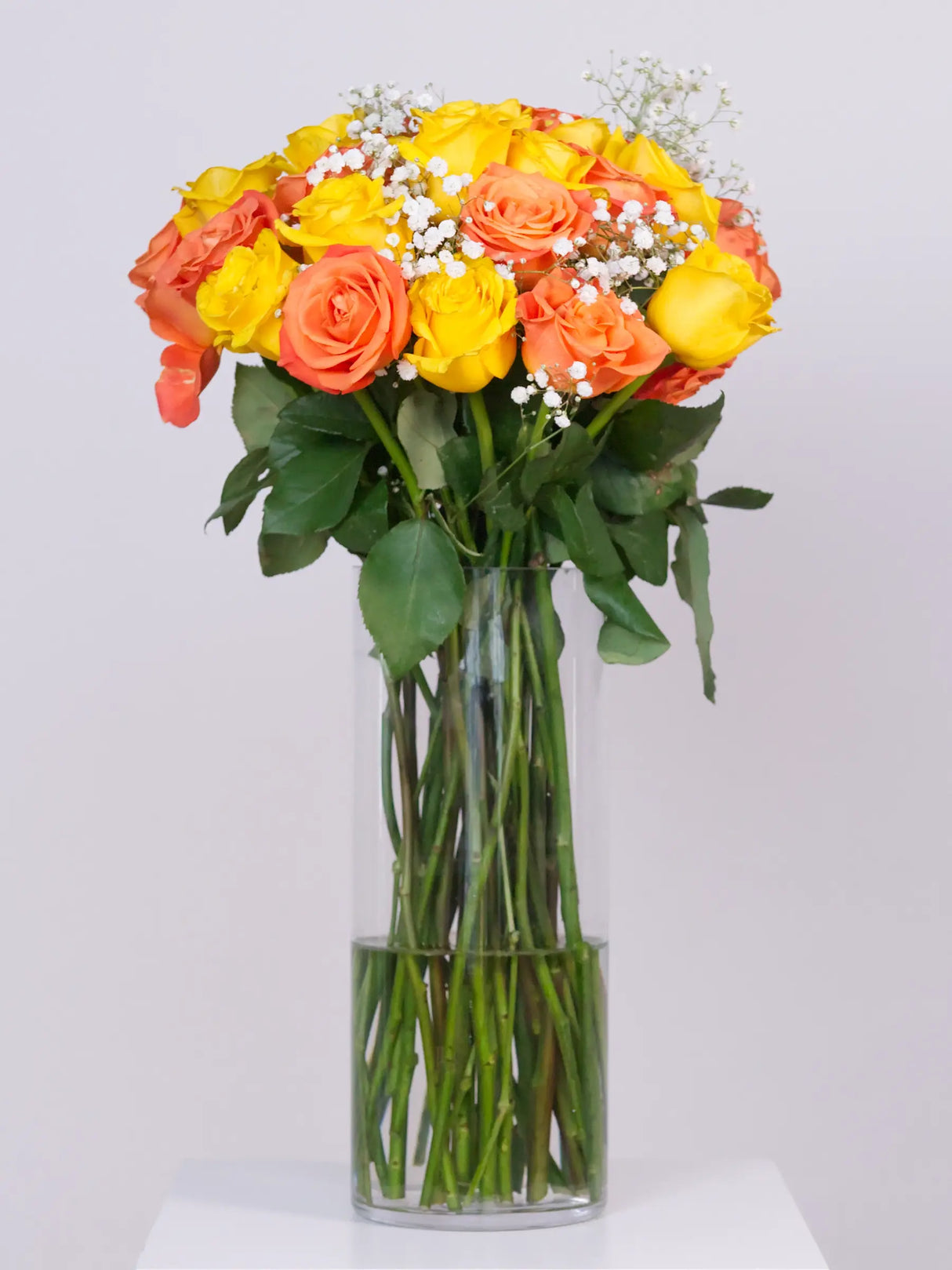 Orange and yellow rose bouquet with gypsophila in tall glass vase
