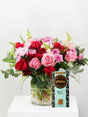 Bouquet of red and pink flowers in a clear vase with a bar of chocolate labeled 'AFRIKOA' on a white surface.