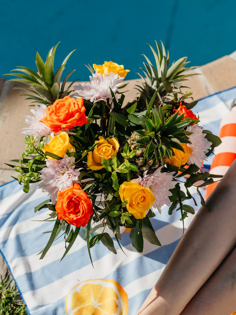 Tropical flower bouquet with fresh pineapples, orange and yellow roses, white chrysanthemums on beach setting - summer holiday arrangement