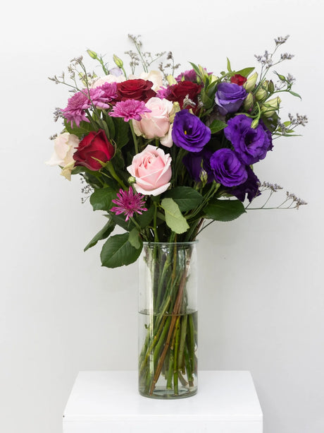 Bouquet of colorful flowers in a clear vase on a white surface with a white background