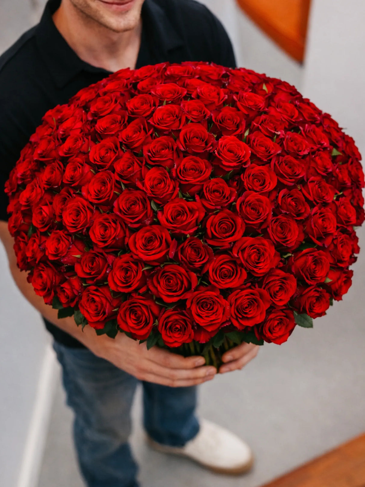 Person holding a large bouquet of red roses against a neutral background