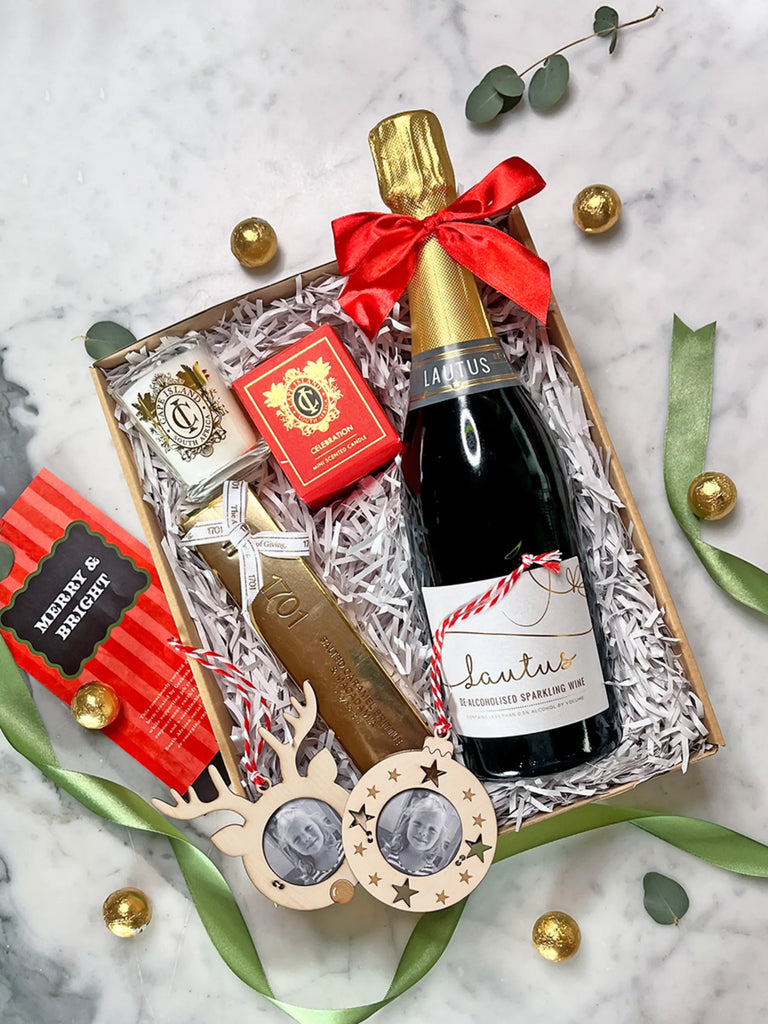 Gift set with a bottle of Lausus sparkling wine, wooden sunglasses, and other items on a marble surface.