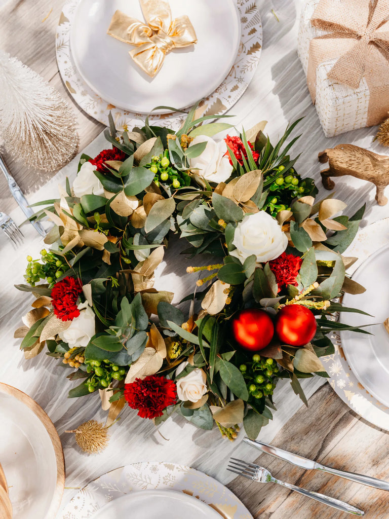 Christmas wreath used as table centrepiece with white roses, red flowers, gold leaves and baubles on elegant dinner table setting