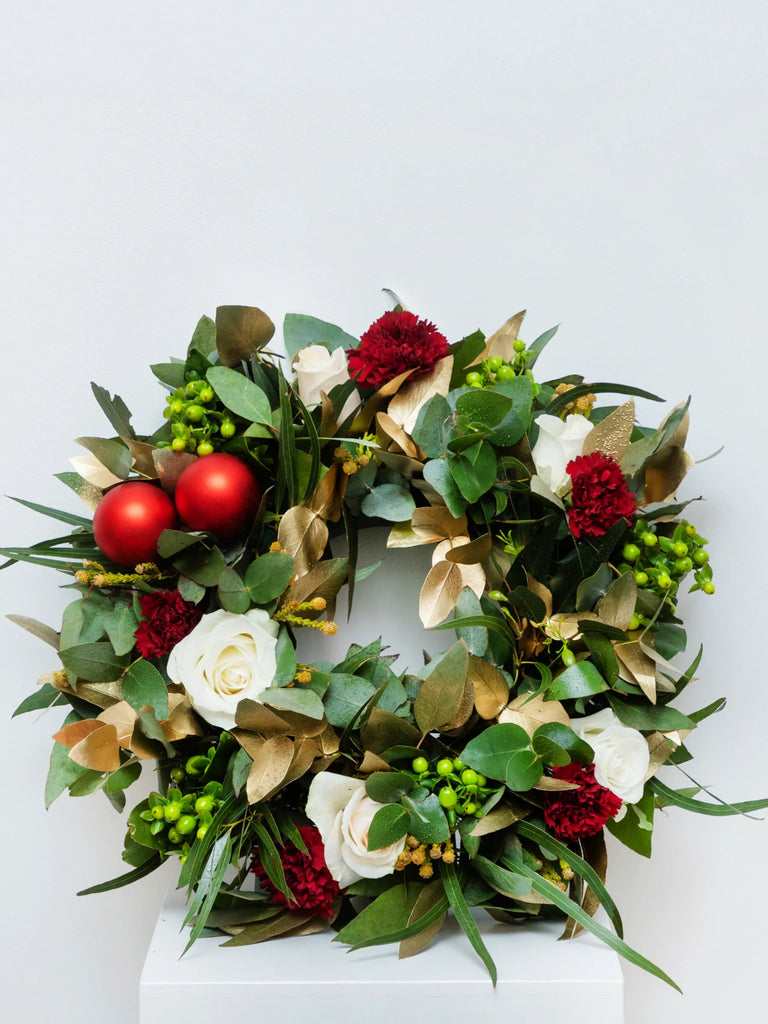 Traditional Christmas wreath with cream roses, red carnations, gold leaves, red baubles and eucalyptus - classic festive door decoration