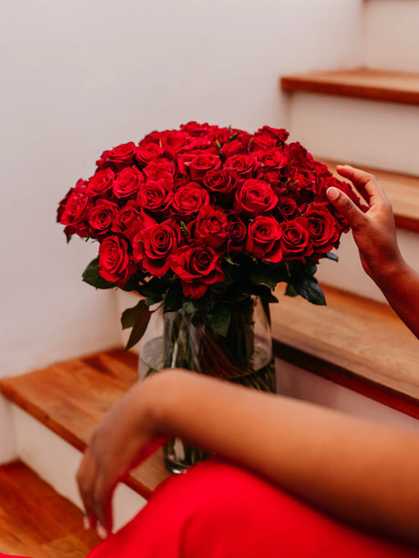 Bouquet of red roses in a vase held by a person on wooden stairs.