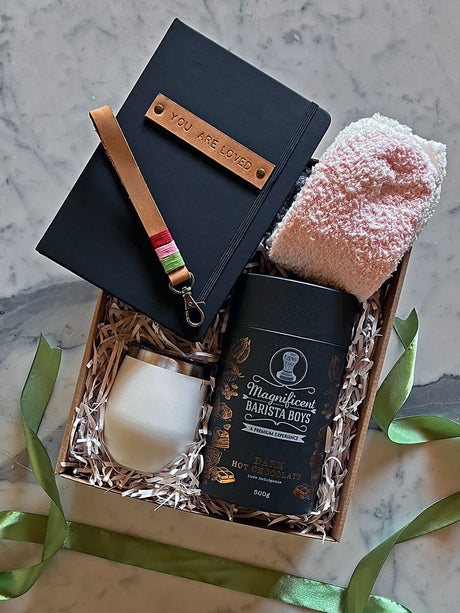 Warm Embrace gift box with hot chocolate, Lizzard tumbler, cozy socks, and a notebook on a marble surface.