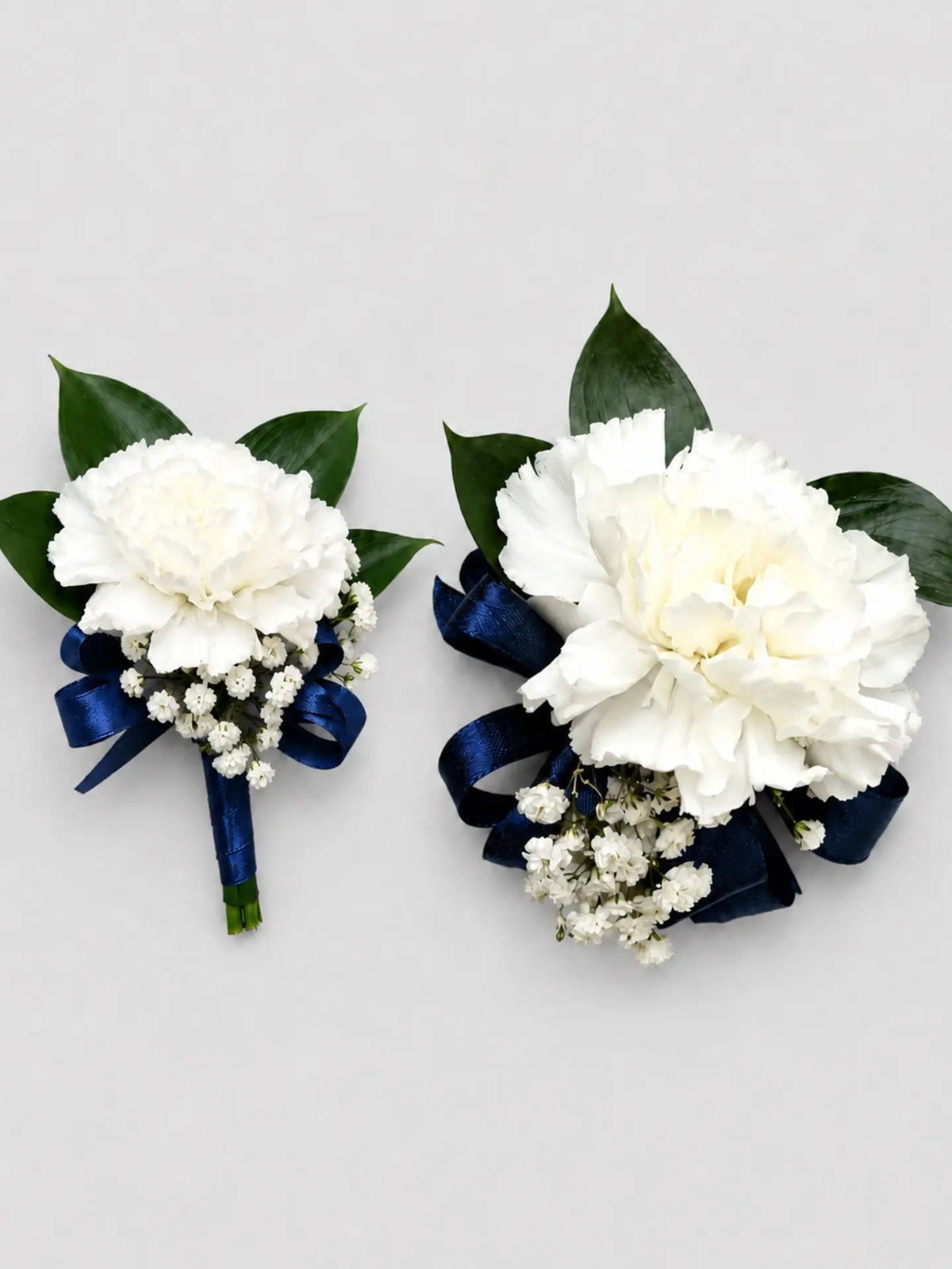 Two white flower corsages with navy ribbons on a light gray background
