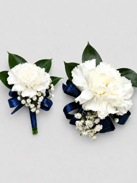 Two white flower corsages with navy ribbons on a light gray background