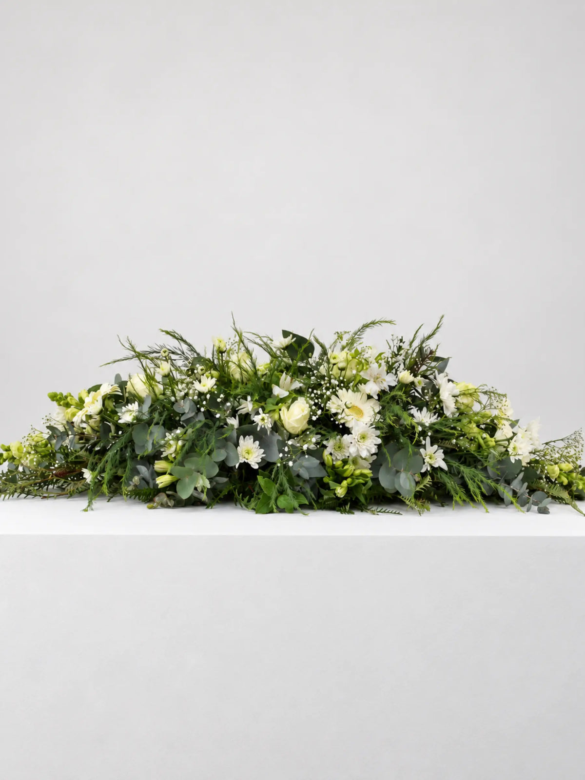 Coffin or Casket Spray of mixed seasonal flowers and greenery for memorial and funeral services.