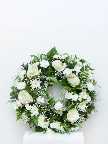 White round wreath featuring mixed seasonal flowers and greenery for a funeral, memorial or sympathy gesture.