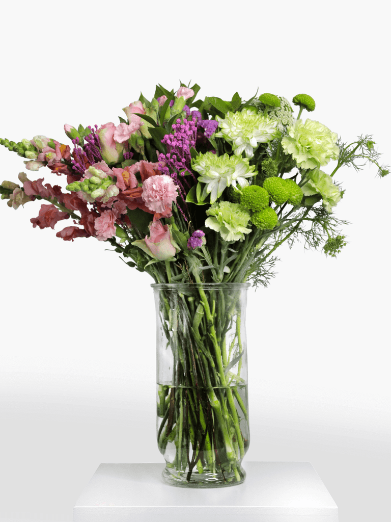 A fresh flower arrangement with green blooms on one side and soft pink blooms on the other, perfectly split in a glass vase.