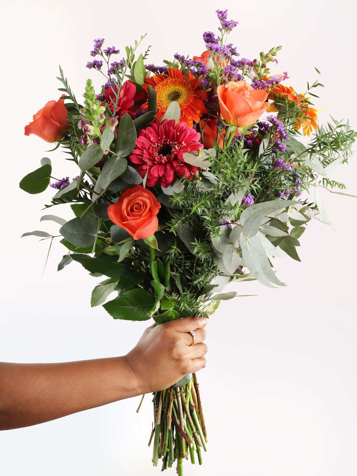 A hand holding a beautiful bouquet of flowers with a variety of colors including pink, orange, and purple, arranged elegantly.