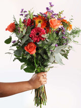 A hand holding a beautiful bouquet of flowers with a variety of colors including pink, orange, and purple, arranged elegantly.