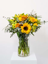 Bright and cheerful bouquet in a clear vase featuring sunflowers and mixed yellow flowers, perfect for gifting to family and friends.