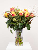 A vibrant orange rose bouquet with greenery, arranged by South African florists, displayed in a clear vase on a white pedestal.