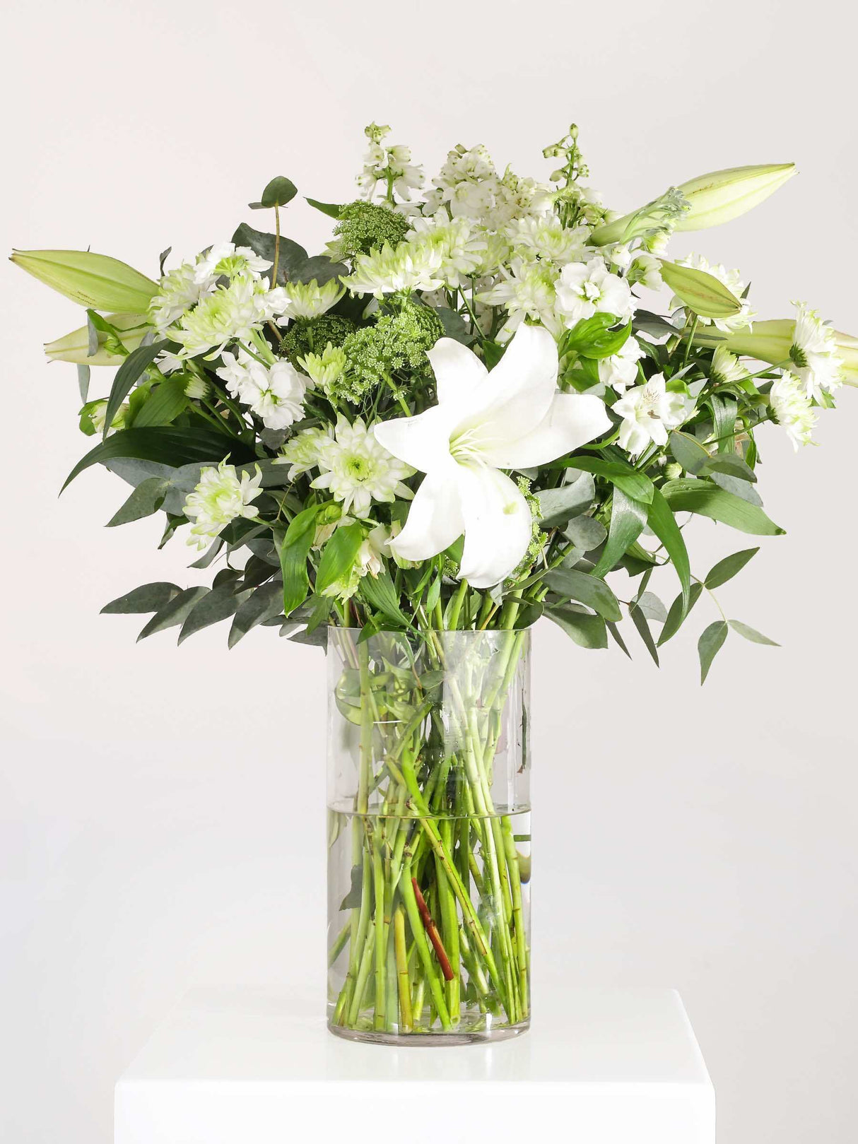 Mixed St Joseph Lily Bunch with seasonal flowers and greenery in a clear vase, showcasing a vibrant floral arrangement.