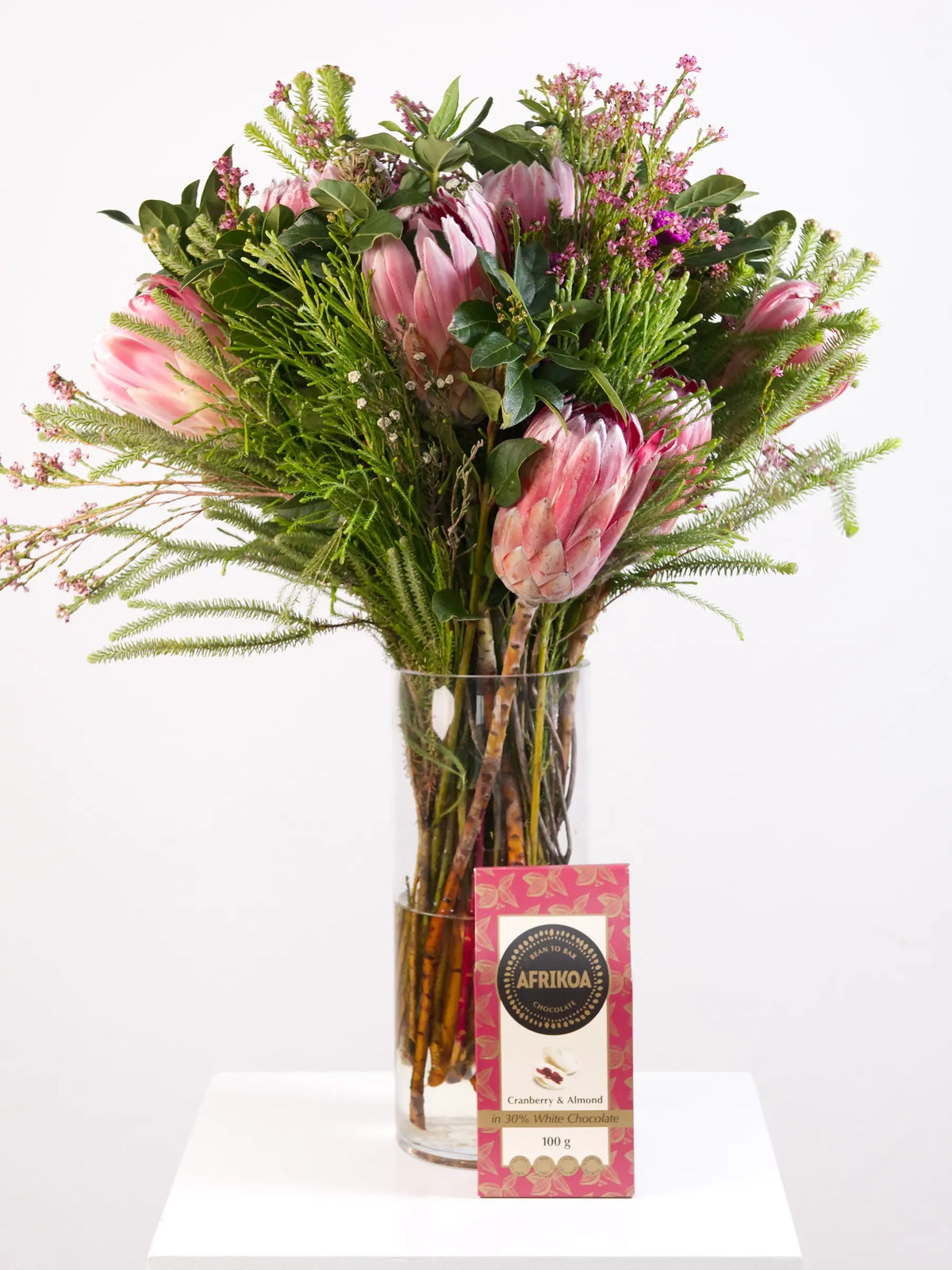 Bouquet of pink flowers in a clear vase with cranberry and almond chocolates on a white background