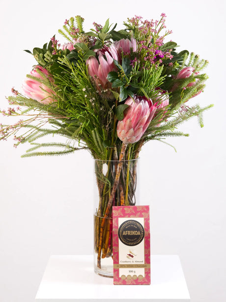 Bouquet of pink flowers in a clear vase with cranberry and almond chocolates on a white background