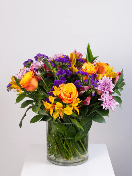 Vibrant mixed flower bouquet with roses, alstroemeria, statice and chrysanthemums in glass vase