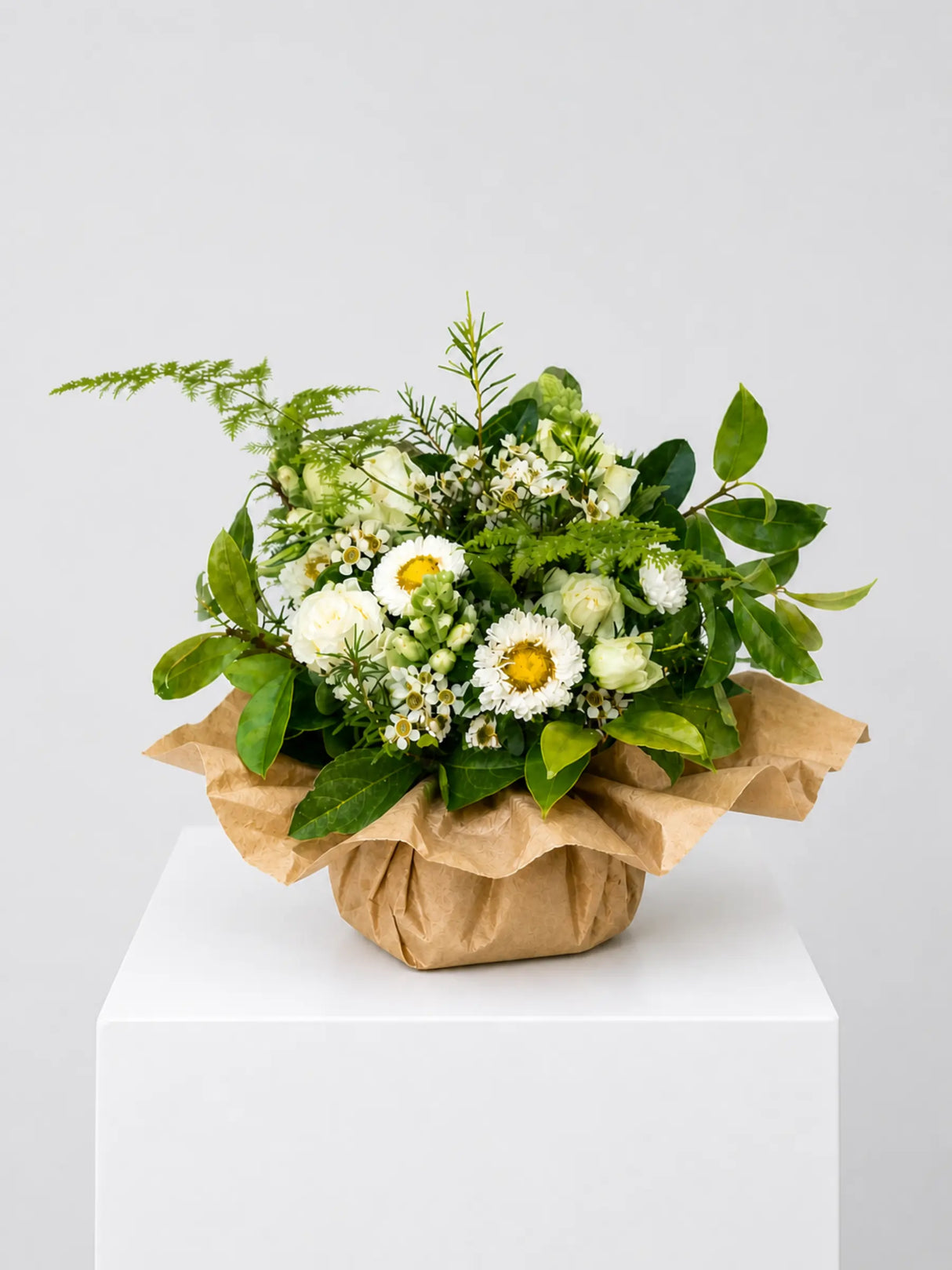 White daisy, spray rose and wax flower arrangement with lush greenery wrapped in kraft paper