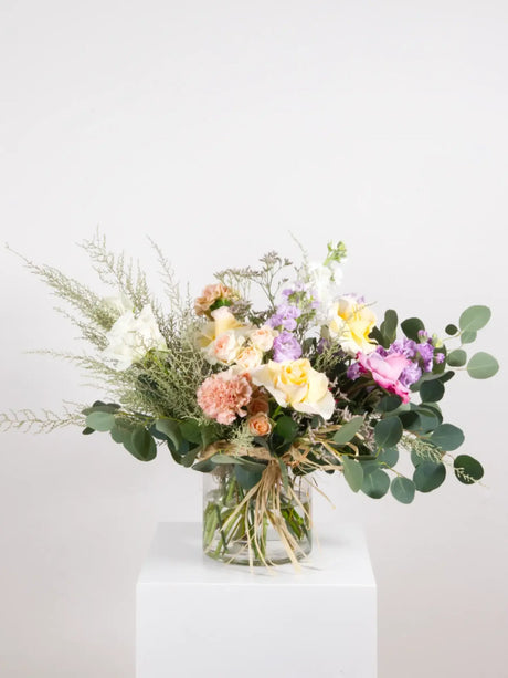 Heartfelt bouquet of pastel seasonal flowers and greenery presented in a glass vase or wrapped in kraft paper to express comfort for the loss of a pet.