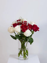 Red and white rose bouquet with baby's breath in a glass vase