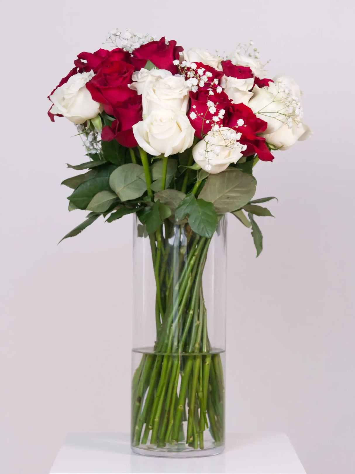 Red and white rose bouquet with baby's breath in a glass vase