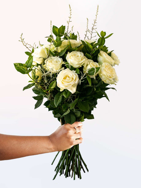 Hand holding a bouquet of white roses and greenery, perfect for a special occasion, with seasonal variations possible.