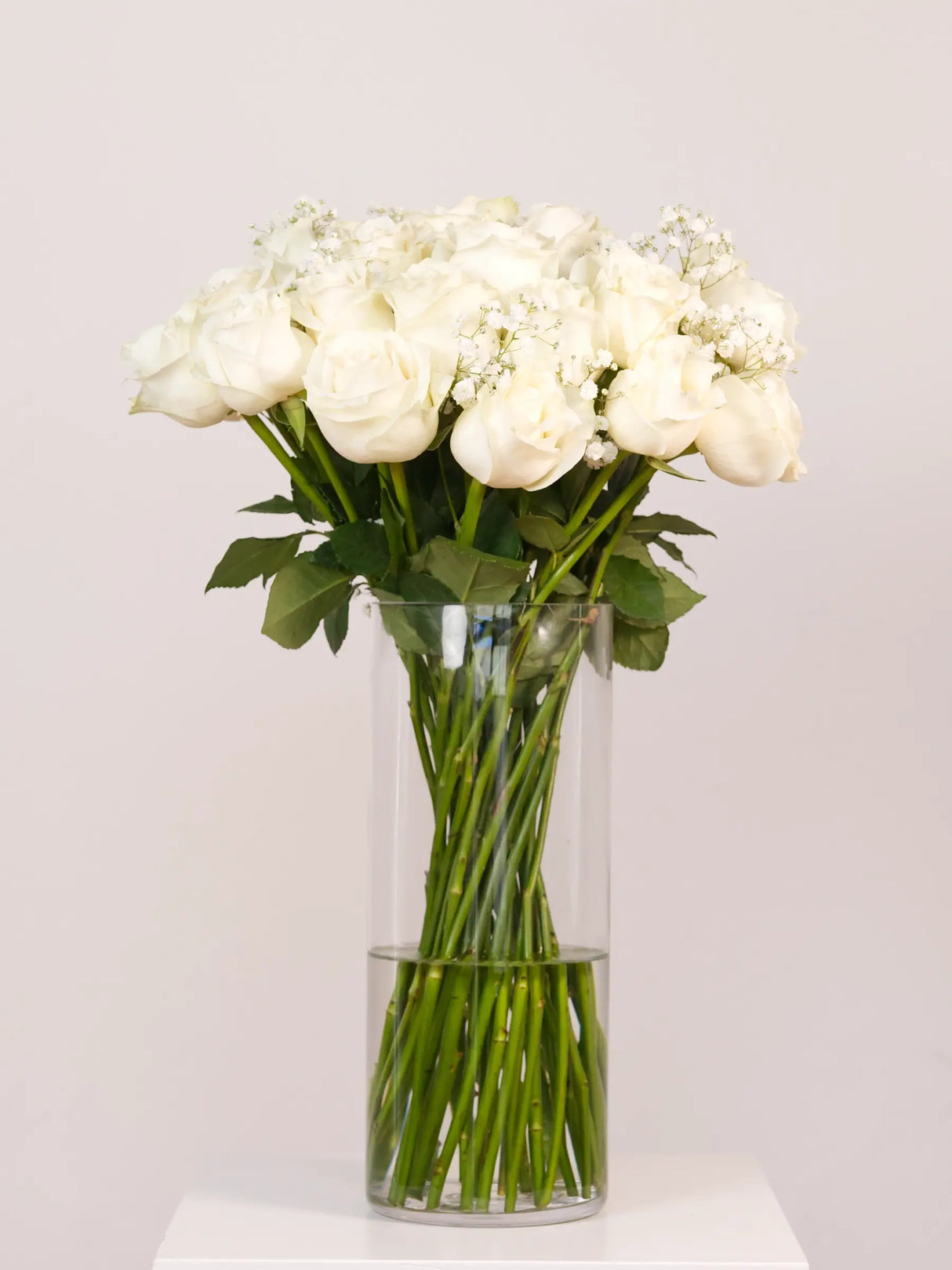 Bouquet of white flowers in a clear vase on a light gray background