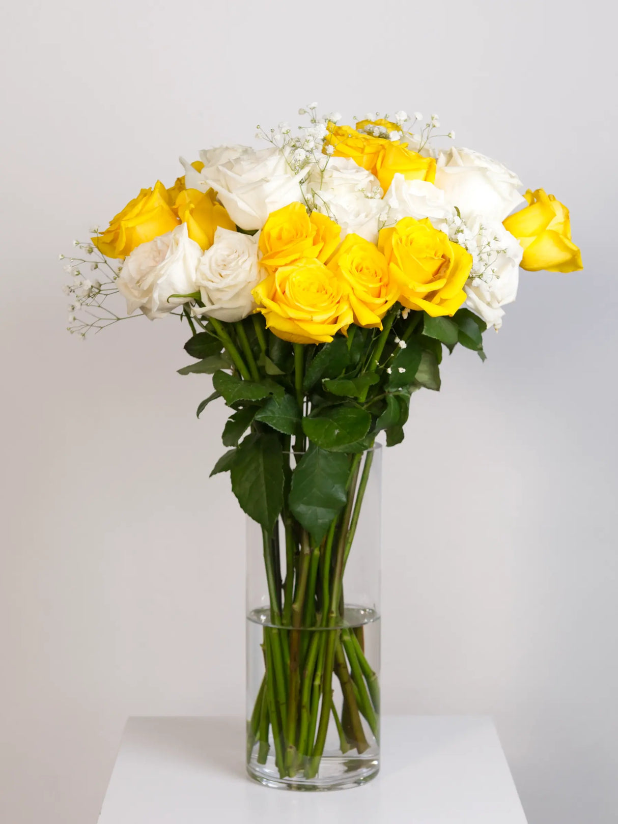 Bouquet of yellow and white flowers in a clear vase on a white background