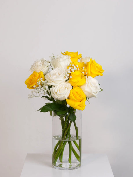 Bouquet of yellow and white roses in a clear vase on a light gray background