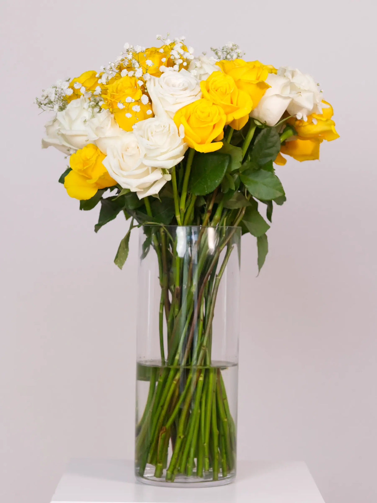 Bouquet of yellow and white flowers in a clear vase on a white background