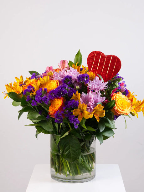 Colorful bouquet of flowers with a red heart-shaped chcolate on a white background