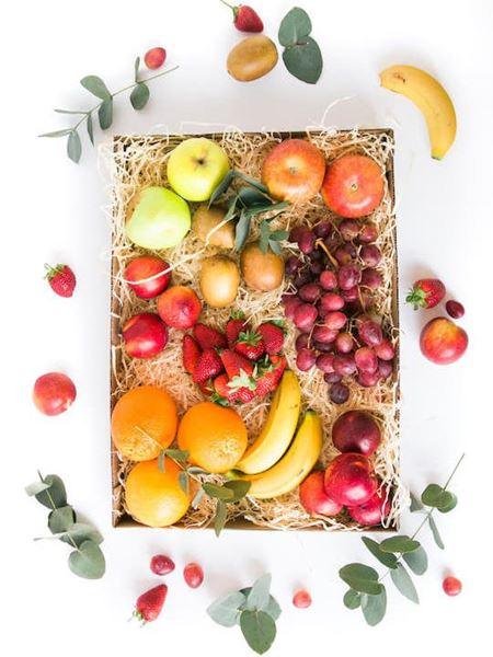 Abundant Fruit Box with fresh apples, bananas, oranges, strawberries, and grapes displayed on natural straw, promoting wellness and vitality.