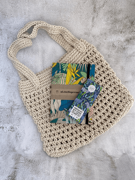 Handcrafted crochet tote with Love Supreme journal and chocolate bar, styled on a textured background. Ideal gift for boho style lovers.