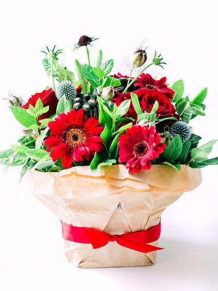 Bouquet inspired by South African veld, featuring red flowers and greenery, wrapped in paper with a red ribbon.