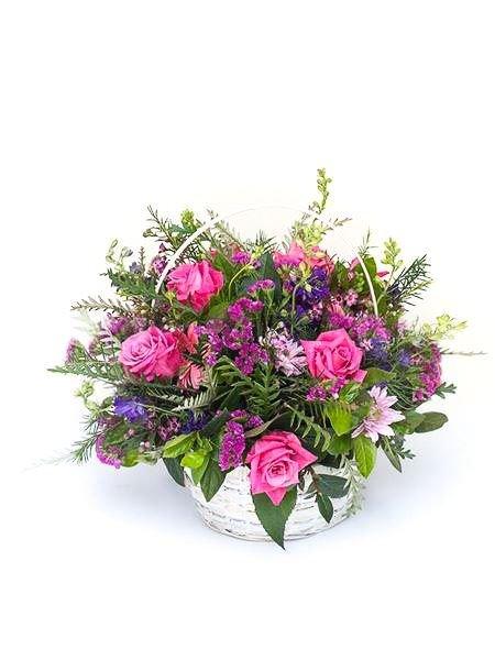 Basket of pink and blue flowers arranged in a celebration theme, featuring roses and assorted seasonal blooms in lush greenery.