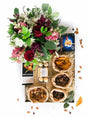 Decadent snack box with biltong, chocolate, nuts, and a vibrant floral arrangement in red, white, and pink hues.