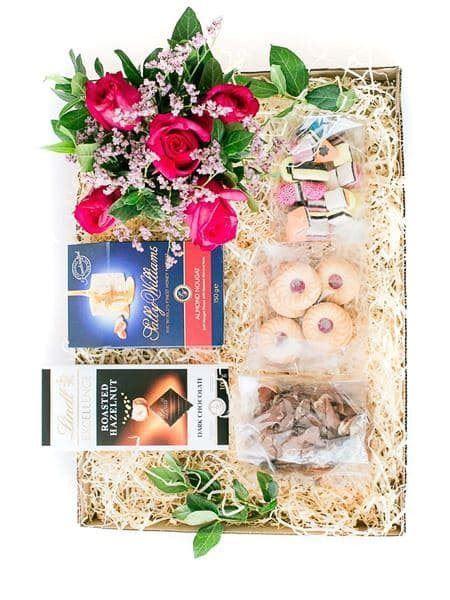 Joyful Gift Box with pink roses, strawberry biscuits, nougat, biltong, liquorice allsorts, and Lindt chocolate on decorative straw.