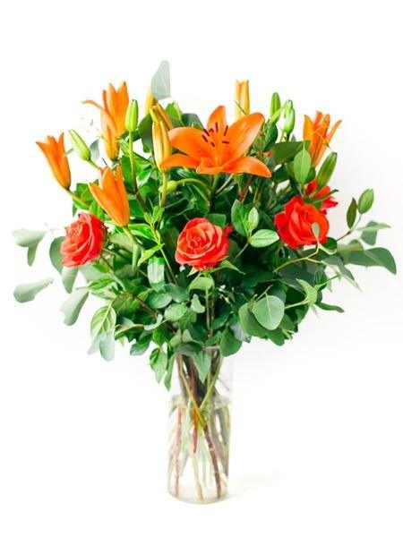 Lilies and roses bouquet in a clear glass vase, featuring lush greenery for a vibrant and elegant floral arrangement.