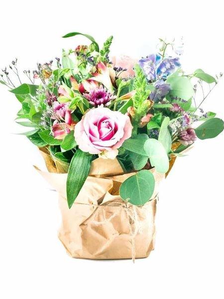 Pastel Posy bouquet with pink roses, blue delphiniums, and greenery in rustic brown wrapping, showcasing a delicate, soft floral arrangement.