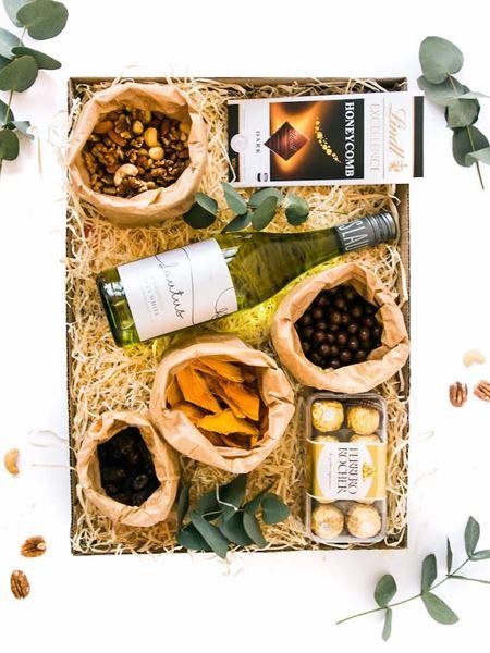 Gift box with non-alcoholic white wine, Lindt chocolate, Ferrero Rocher, mixed nuts, dried fruit, and snacks, elegantly presented.