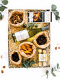 Gift box with non-alcoholic white wine, Lindt chocolate, Ferrero Rocher, mixed nuts, dried fruit, and snacks, elegantly presented.
